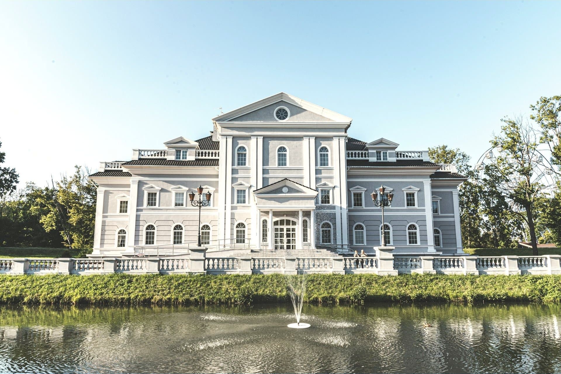 A white neoclassical estate reflected in a pond with a fountain