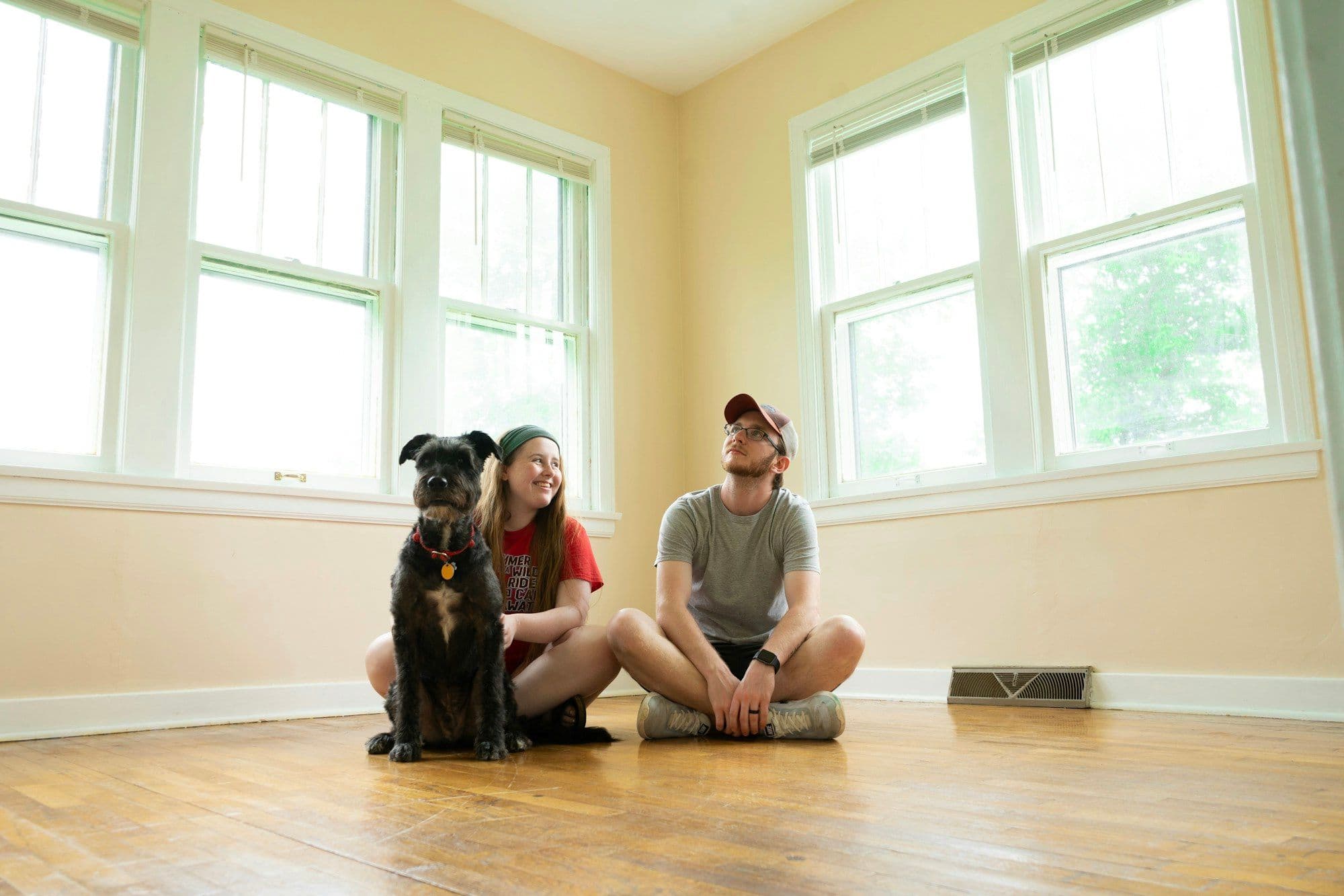 A couple and their dog sitting on the floor of a sunny, empty new home